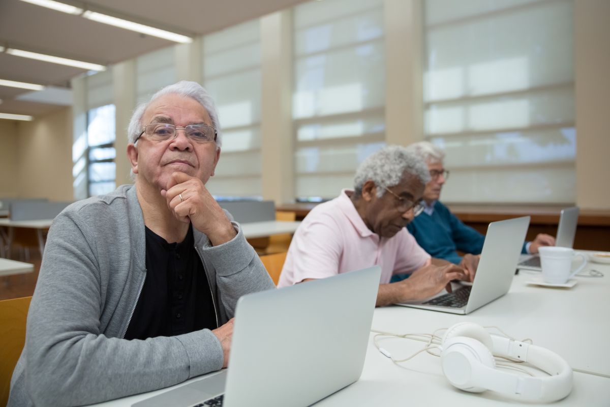 Twee senioren werken op een laptop terwijl iemand meekijkt en uitleg geeft